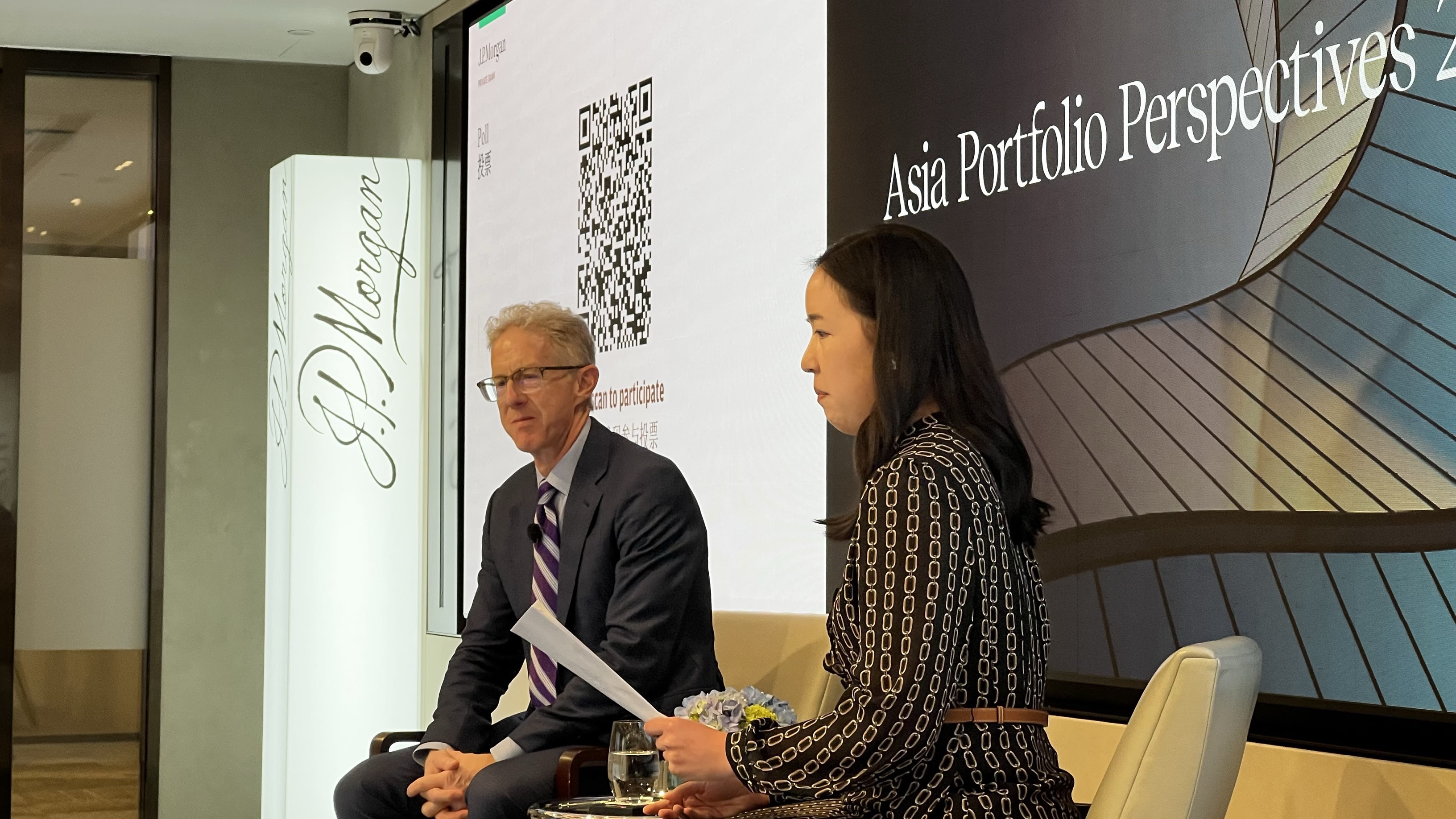 two men and woman sat in chairs on stage in conversation