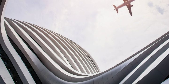 Photograph of an airplane soaring over a building.